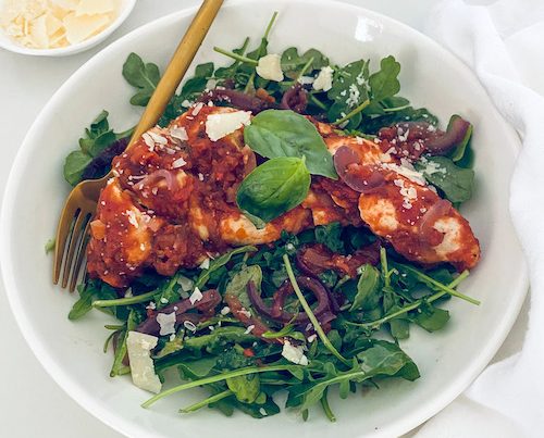 Balsamic chicken over mixed greens on a white plate.