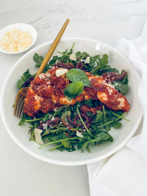 Balsamic chicken over mixed greens on a white plate.