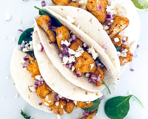 Cauliflower taco filling in flour tortillas with lime wedges.