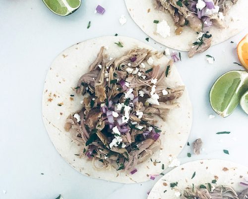 Chicken carnitas on flour tortillas on a white surface.
