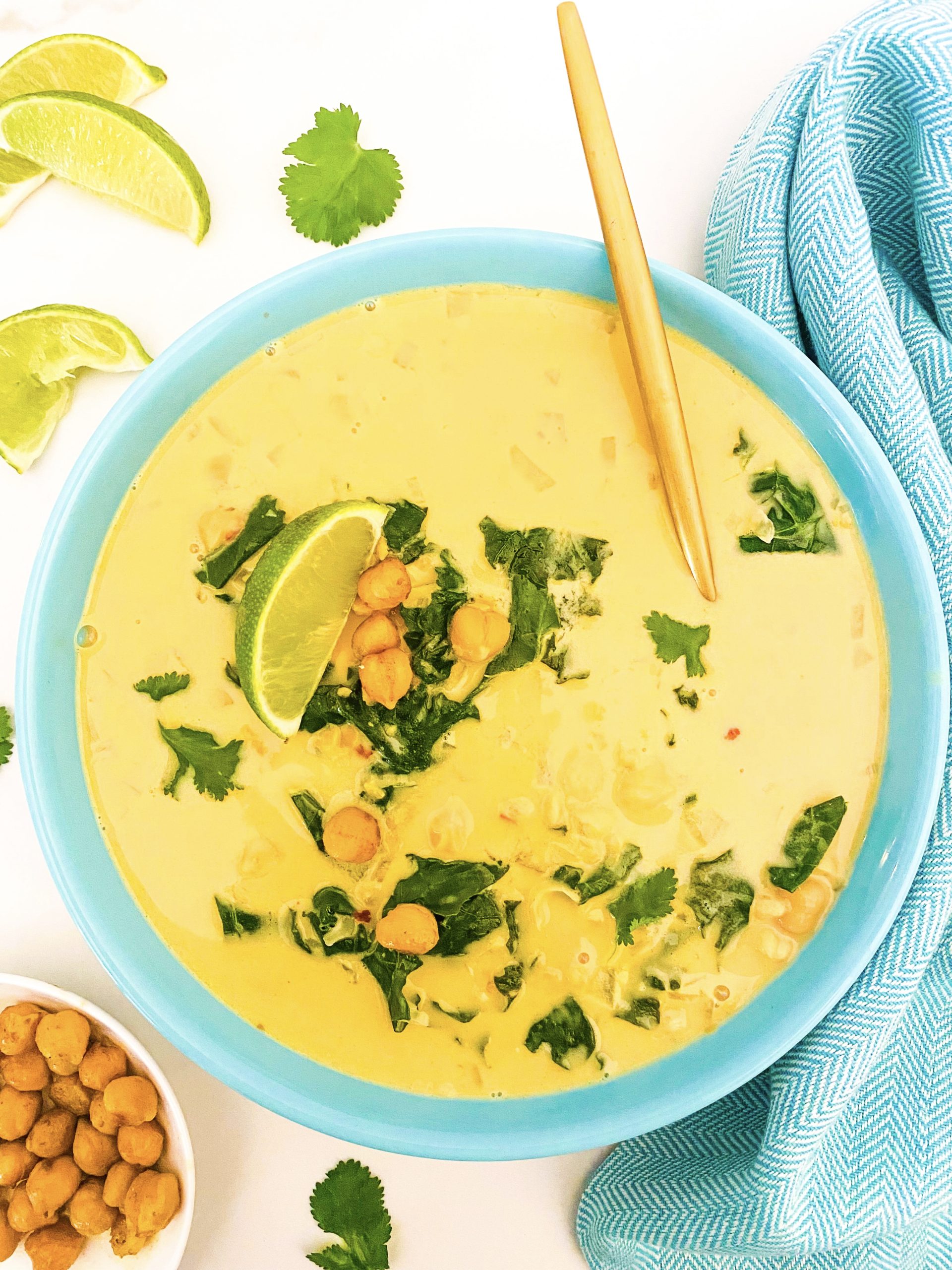 Creamy chickpea kale coconut soup in a blue bowl with a gold spoon.