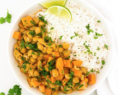 Chickpea and sweet potato tikka next to rice in a white bowl.