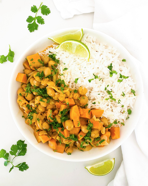 Chickpea and sweet potato tikka next to rice in a white bowl.