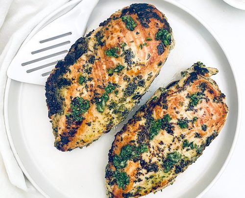 Two chimichurri chicken breasts on a plate.