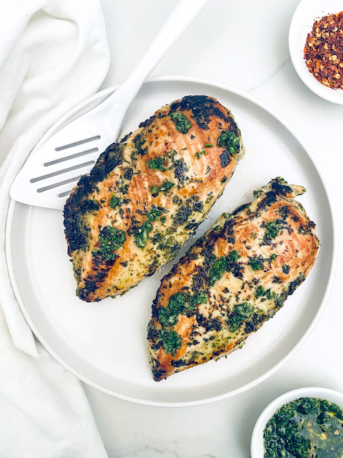 Two chimichurri chicken breasts on a plate.