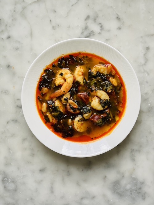 A white bowl of chorizo, shrimp, and white bean stew.