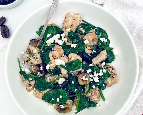 A white bowl and fork with citrus Greek Chicken and spinach.