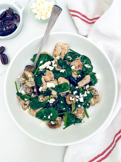 A white bowl and fork with citrus Greek Chicken and spinach.