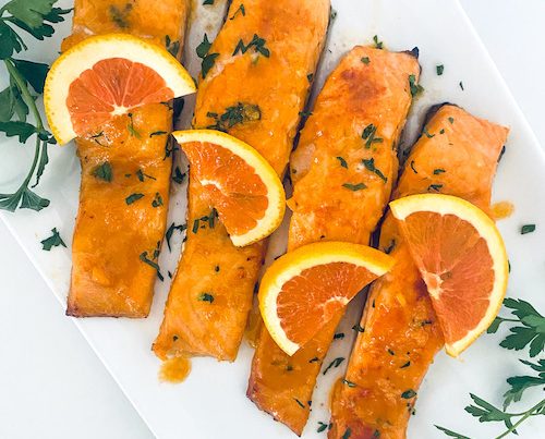 Salmon filets topped with orange slices on a white platter.