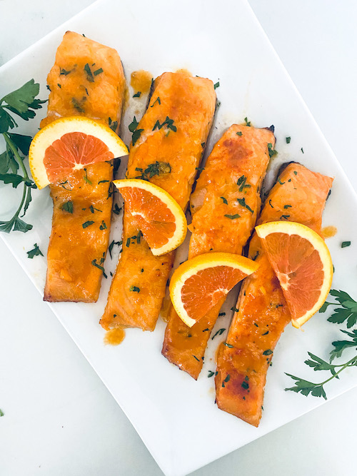 Salmon filets topped with orange slices on a white platter.