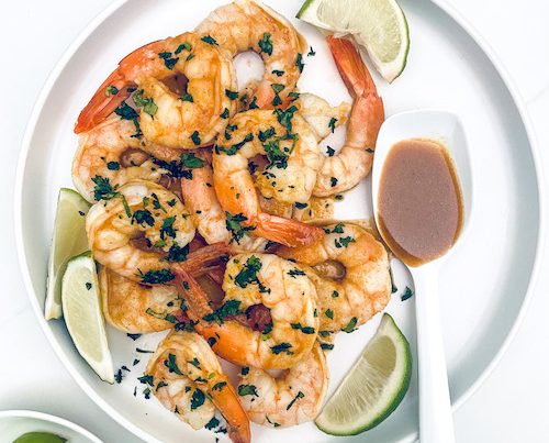 Citrus grilled shrimp and lime wedges on a white plate.