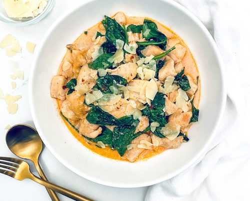 A white bowl filled with creamy parmesan chicken and spinach.