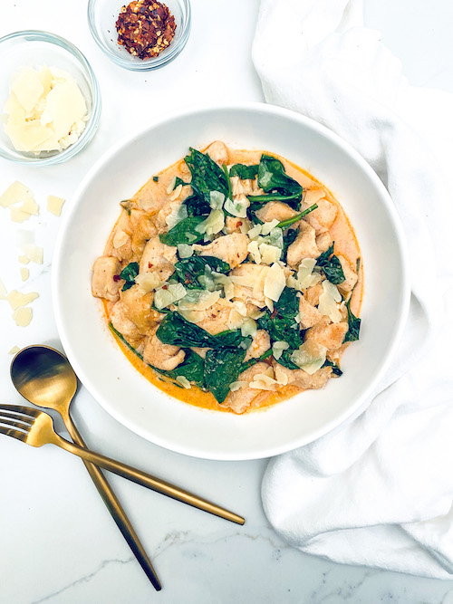 A white bowl filled with creamy parmesan chicken and spinach.