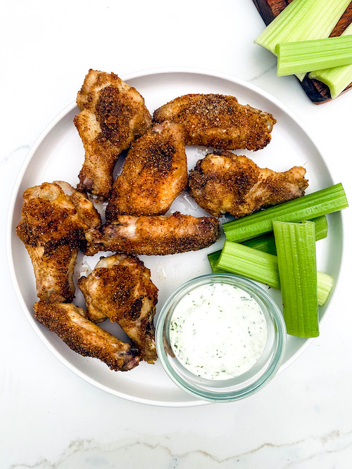 Crispy cumin chicken wings with celery on a plate.