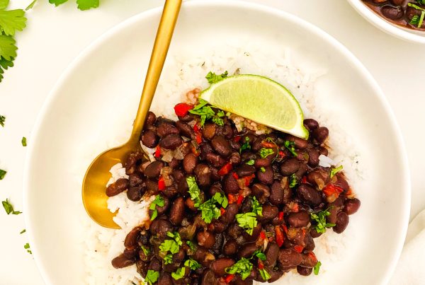 Cuban black beans over rice with lime wedges in a white bowl.