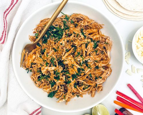 A white serving bowl of shredded enchilada chicken.