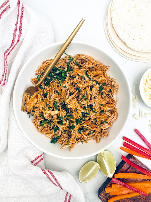 A white serving bowl of shredded enchilada chicken.