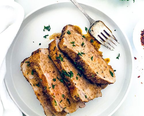 Slices of garlic balsamic pork loin with a fork on a white plate.
