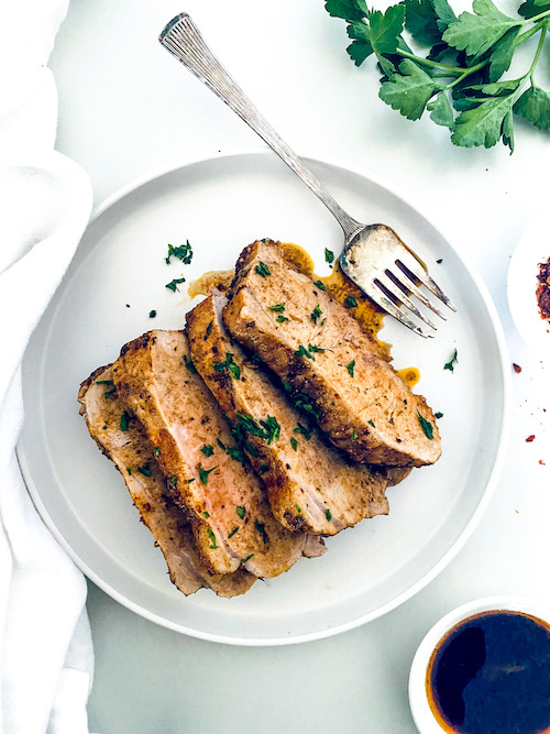 Slices of garlic balsamic pork loin with a fork on a white plate.