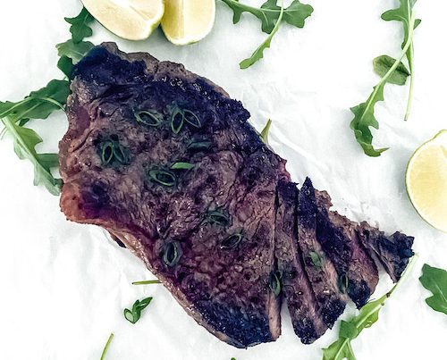 Garlic soy grilled steak on a white surface with lime wedges.