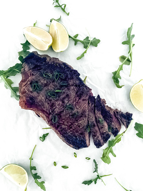 Garlic soy grilled steak on a white surface with lime wedges.