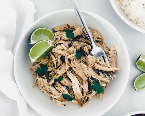 Garlic Cuban pulled chicken with lime wedges in a white bowl.