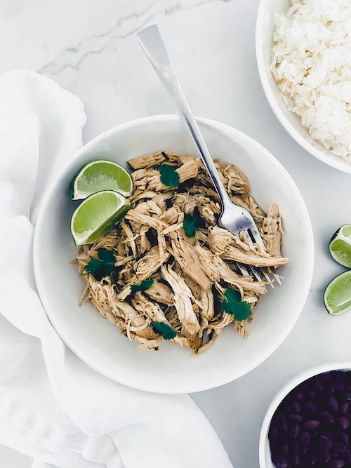 Garlic Cuban pulled chicken with lime wedges in a white bowl.