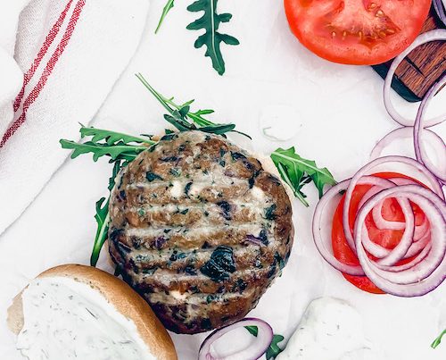A Greek turkey burger on a bun with tomatoes and red onions.