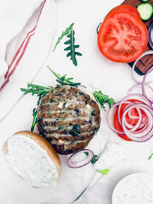 A Greek turkey burger on a bun with tomatoes and red onions.