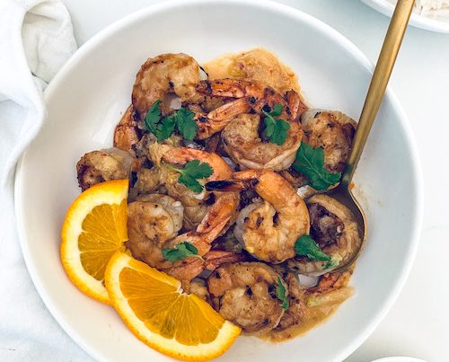 Honey garlic Korean shrimp with orange wedges in a white bowl.