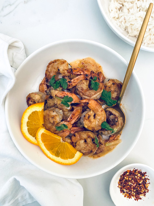 Honey garlic Korean shrimp with orange wedges in a white bowl.