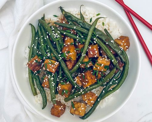 Honey soy tempeh with green beans over rice in a white bowl.