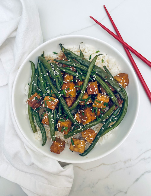 Honey soy tempeh with green beans over rice in a white bowl.