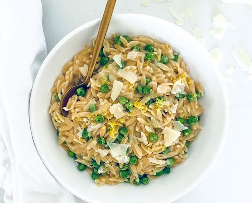 A white bowl filled with lemon Parmesan orzo and peas.