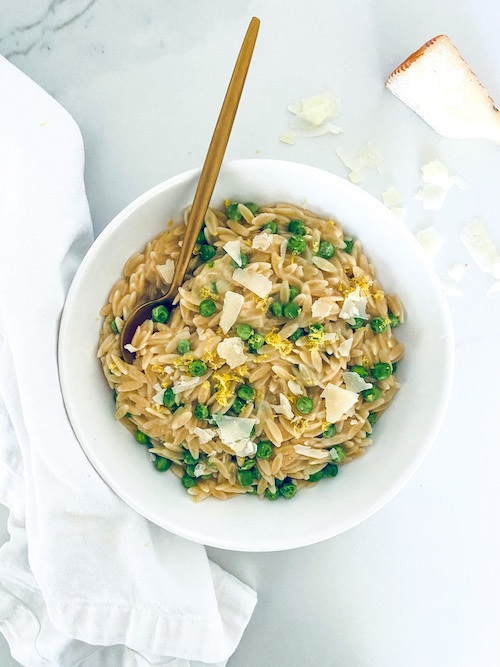 A white bowl filled with lemon Parmesan orzo and peas.