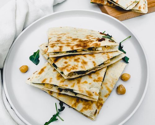 Mediterranean quesadilla triangles stacked on a white plate.