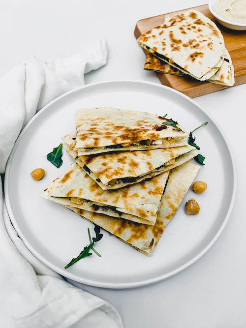 Mediterranean quesadilla triangles stacked on a white plate.