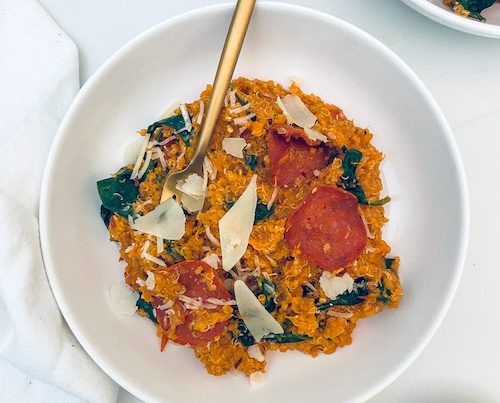 Pizza flavored quinoa with a gold fork in a white bowl.