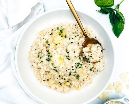 A white bowl with golden spoon filled with vegetarian risotto.