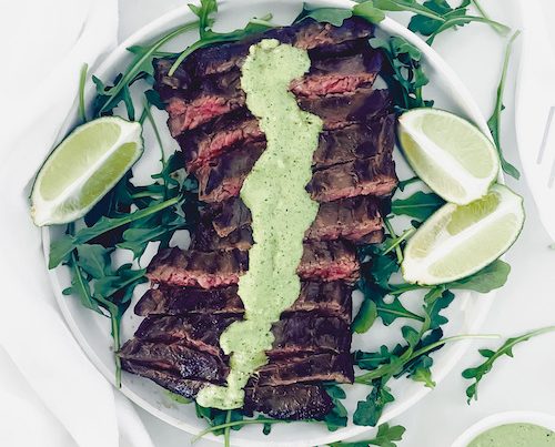 Skirt steak with cream sauce and limes on a white plate.