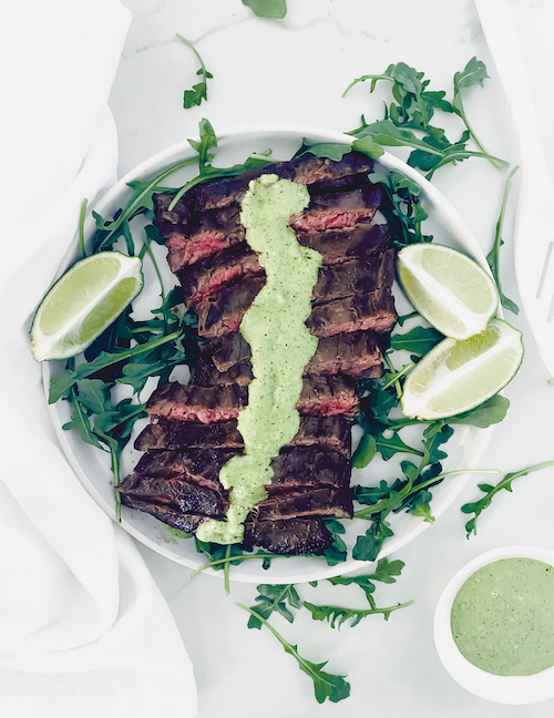 Skirt steak with cream sauce and limes on a white plate.