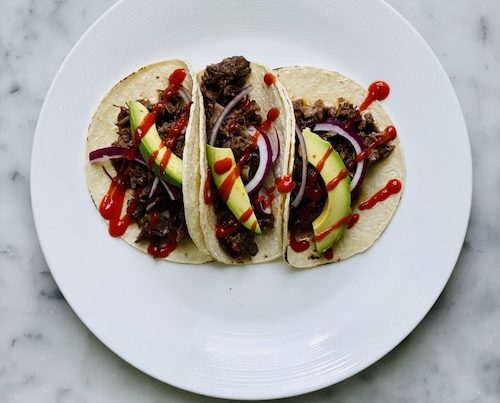 Sriracha brown sugar short rib tacos with avocado on a white plate.