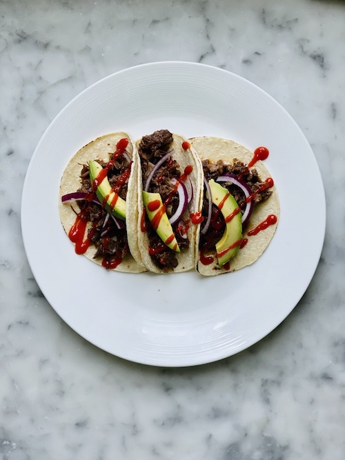 Sriracha brown sugar short rib tacos with avocado on a white plate.