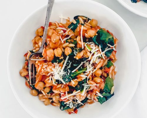 Tuscan orzo with chickpeas and a fork in a white bowl.