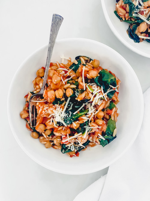 Tuscan orzo with chickpeas and a fork in a white bowl.