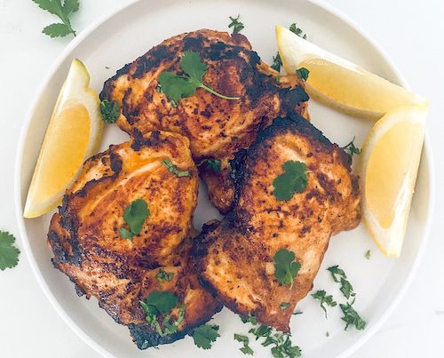 Yogurt Marinated Chicken with lemon wedges on a white plate.