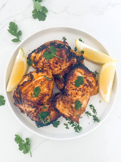 Yogurt Marinated Chicken with lemon wedges on a white plate.