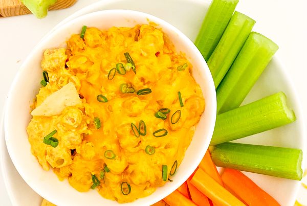 A small bowl of creamy buffalo chickpea dip next to a plate of celery and carrots.