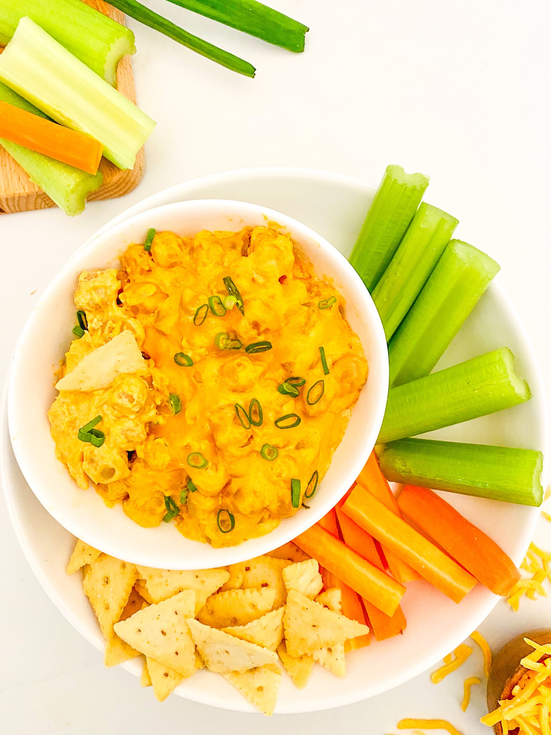 A small bowl of creamy buffalo chickpea dip next to a plate of celery and carrots.