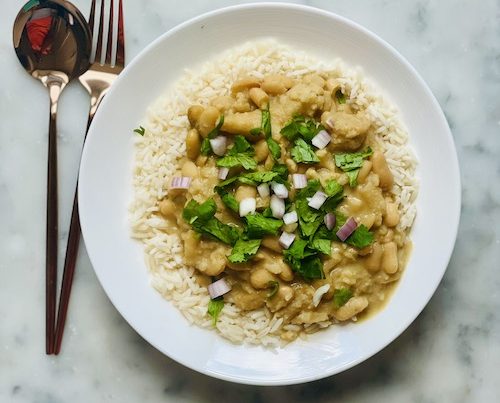 A white bowl of coconut white bean and cauliflower over rice.
